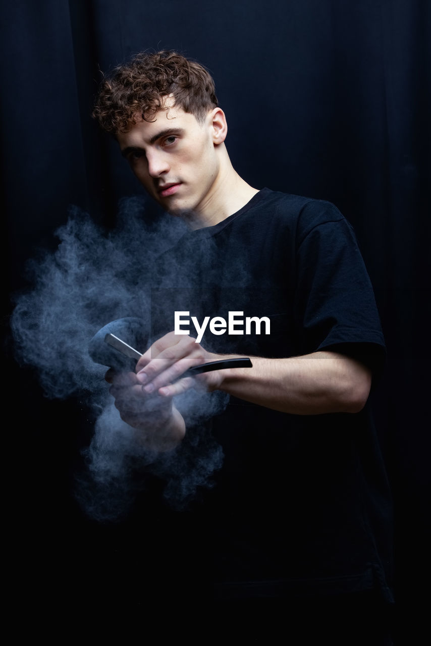 Portrait of young man holding razor against black background