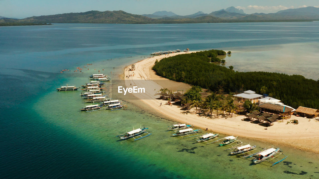 Tropical island and sandy beach with tourists surrounded by coral reef and blue sea in honda bay