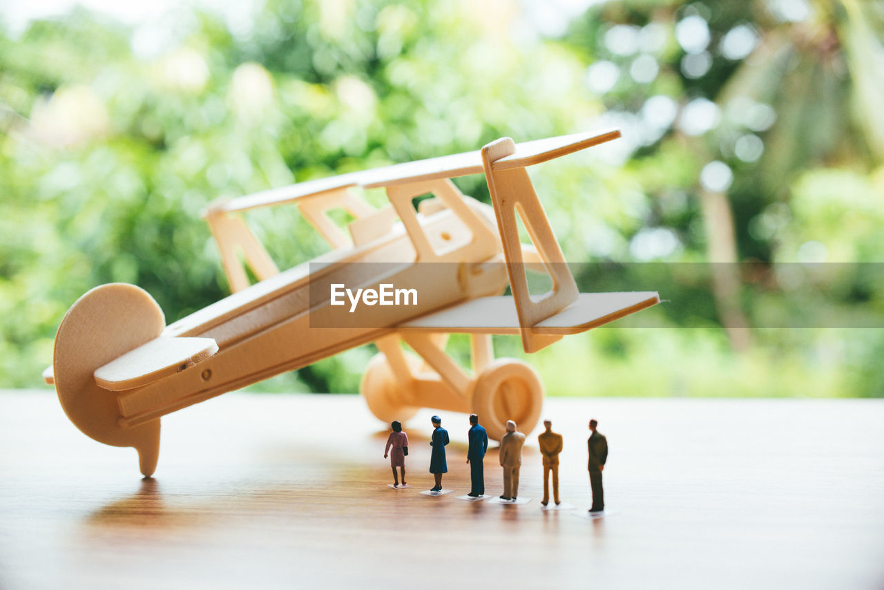 Close-up of toy airplane with figurines on wooden table against trees