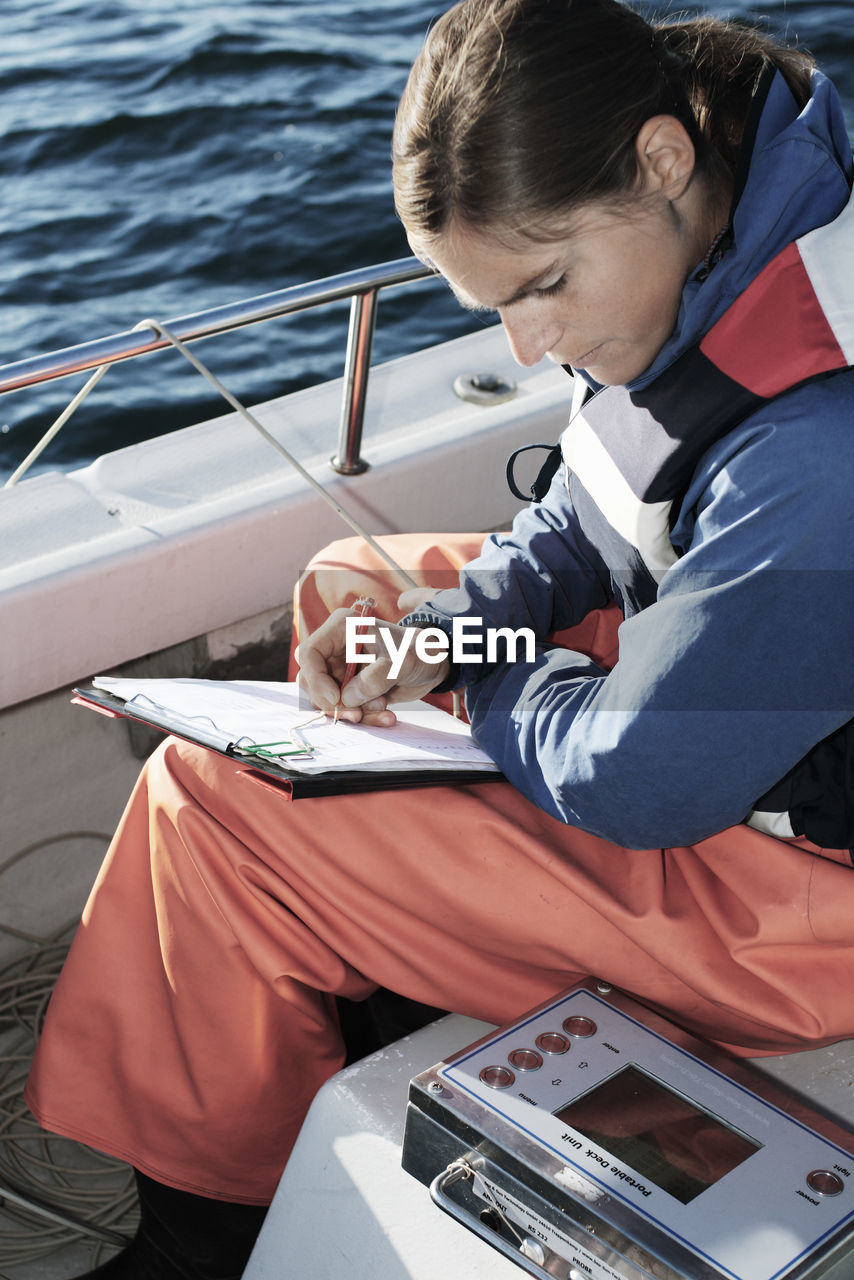 High angle view of woman examining while writing on clipboard in boat
