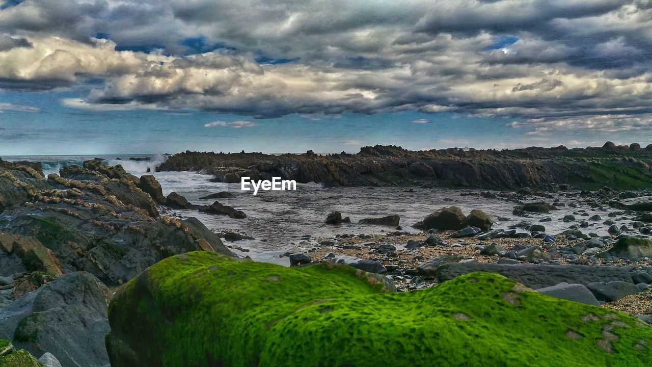SCENIC VIEW OF ROCK FORMATION BY SEA AGAINST CLOUDY SKY
