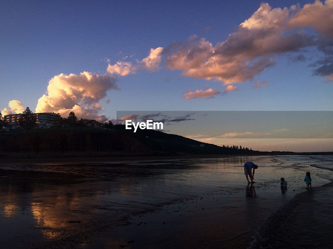 Father with children on beach against sky during sunset