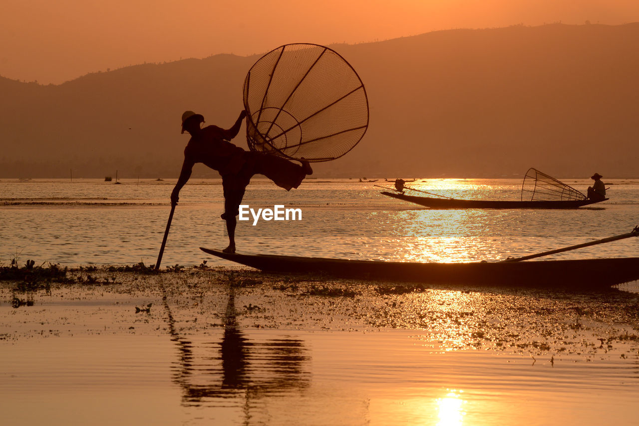 Fisherman fishing in lake with conical fishing nets during sunset