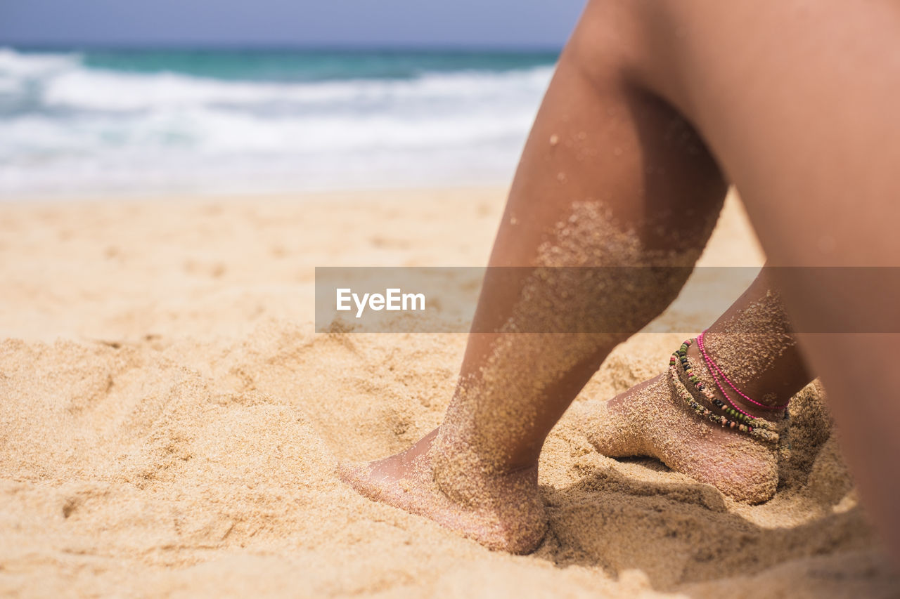 Low section of woman on sand at beach