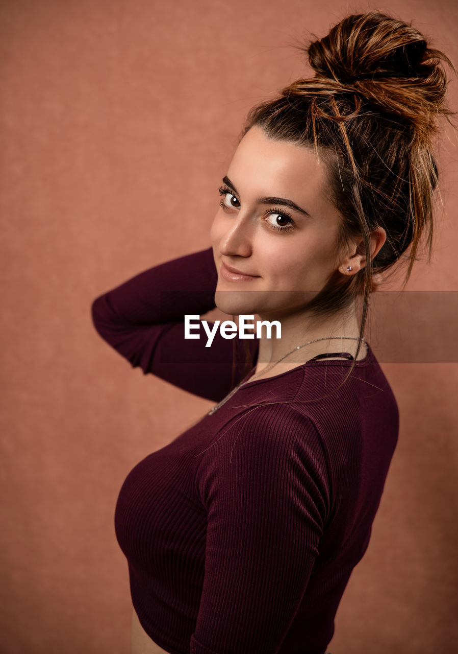 PORTRAIT OF YOUNG WOMAN WITH ARMS RAISED STANDING AGAINST WALL