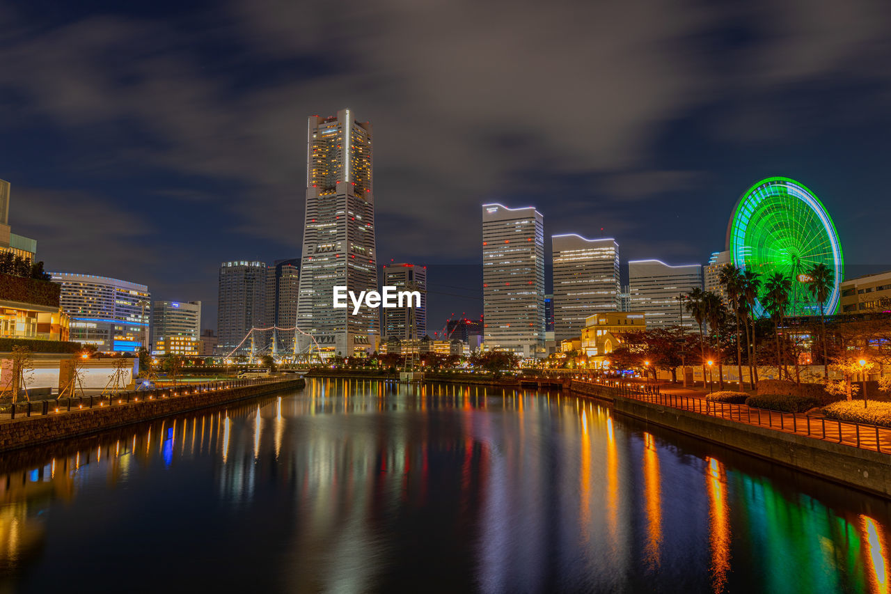 Illuminated modern buildings by river against sky at night in yokohama 