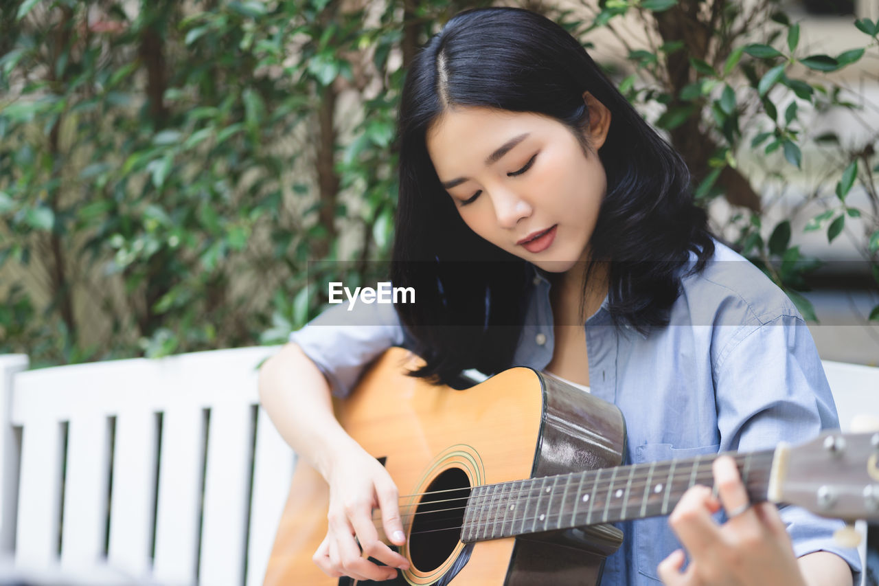 Young woman playing guitar while sitting in park