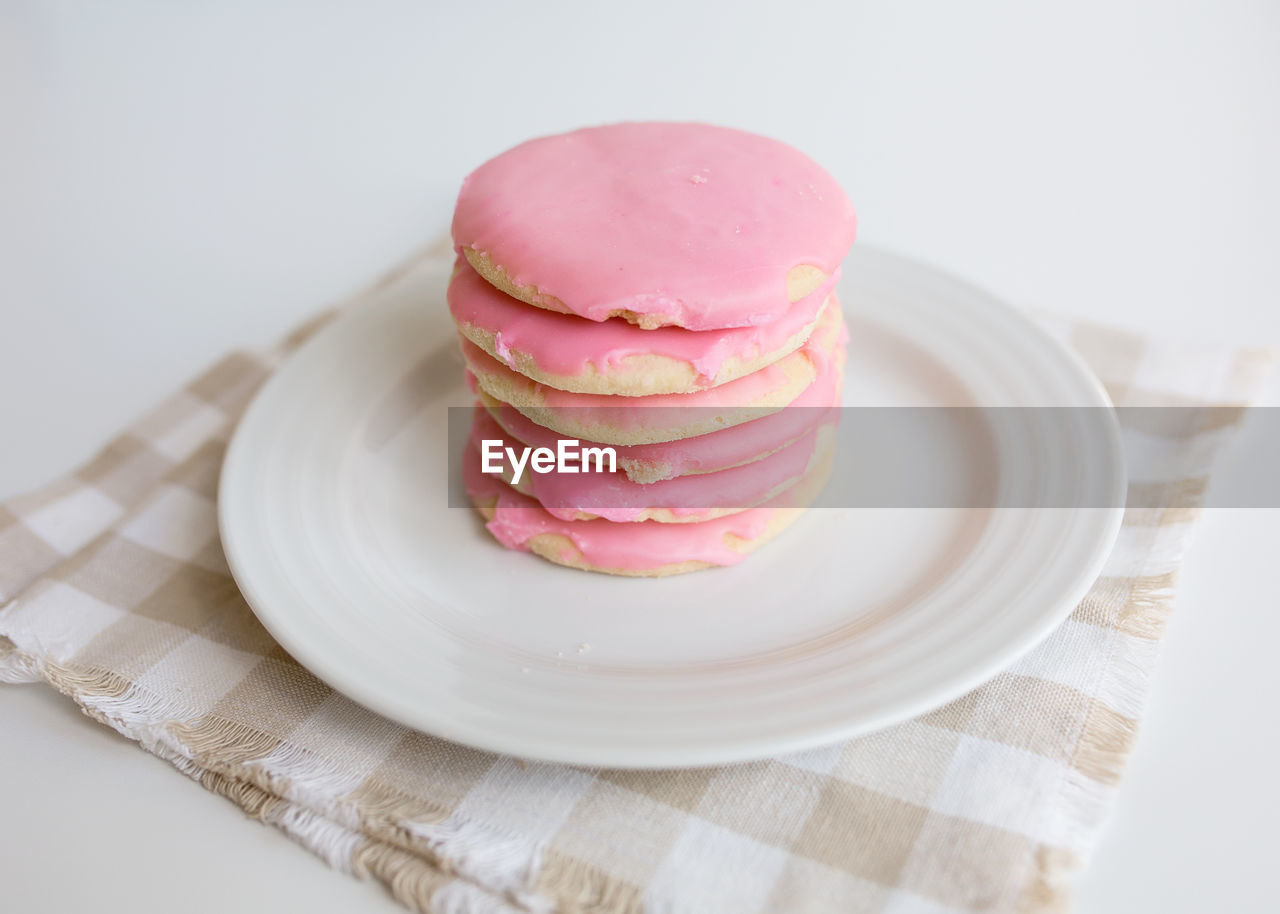 Stack of pink frosted sugar cookies on white plate with neutral colors