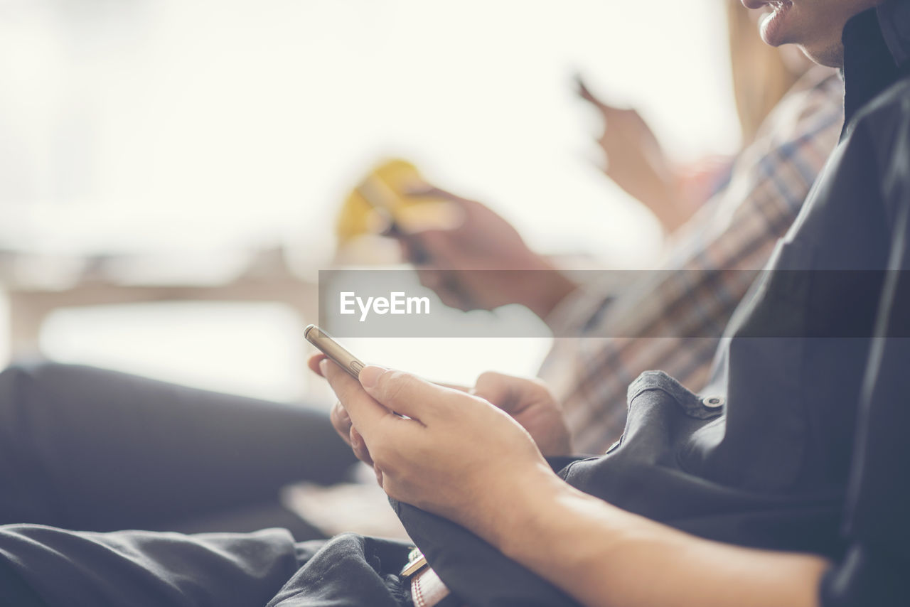 Midsection of man using mobile phone while sitting indoors