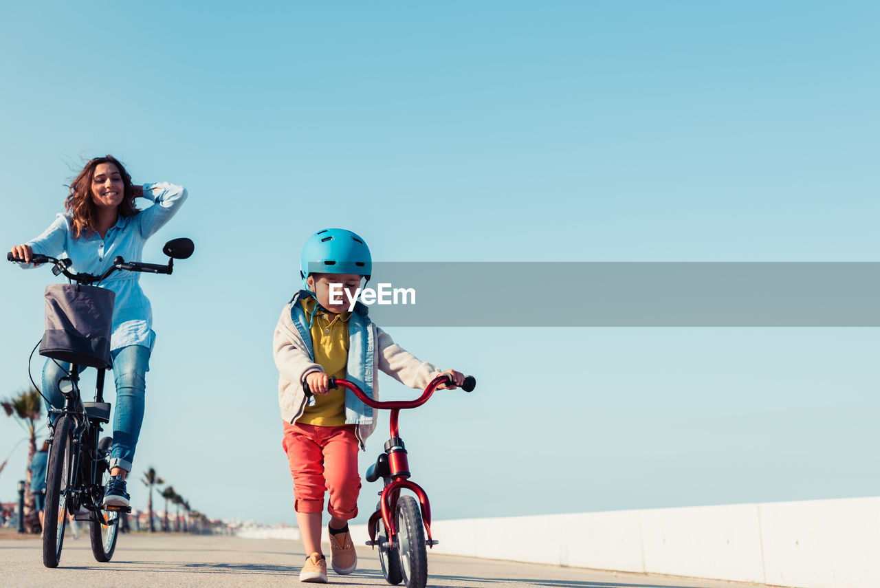 Little kid riding a balance bike with his mother on a bicycle in a city park