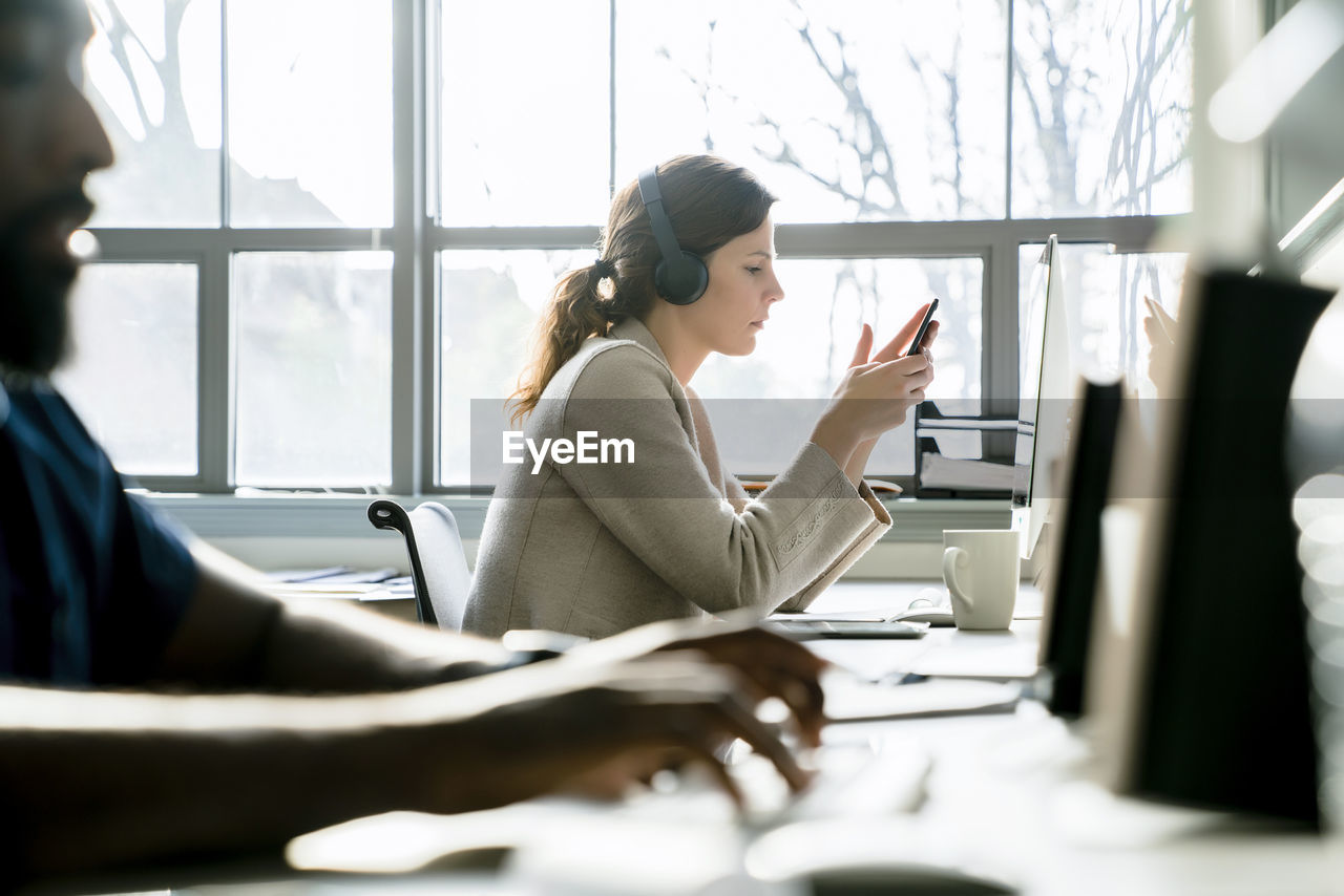 Businesswoman using smart phone while sitting by colleague in office