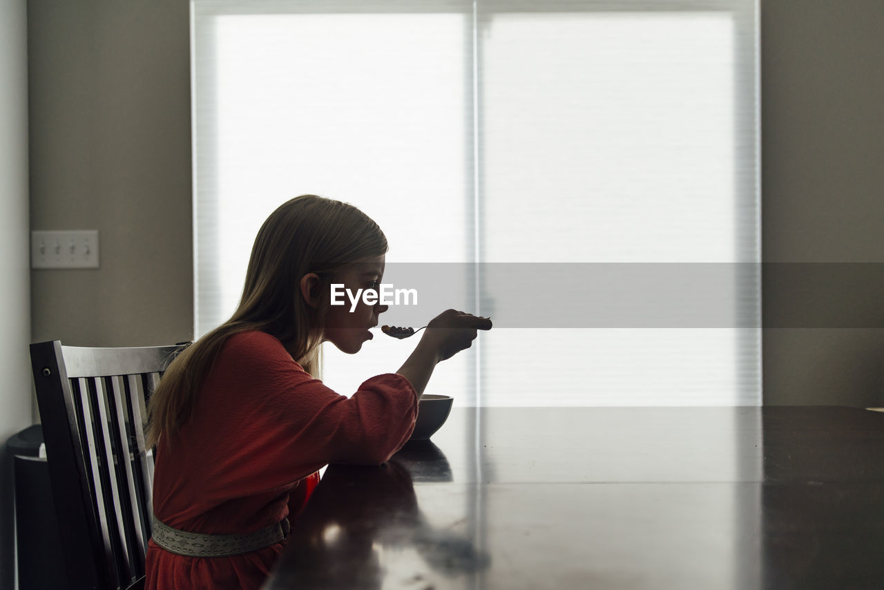 Side view of girl eating food while sitting at home