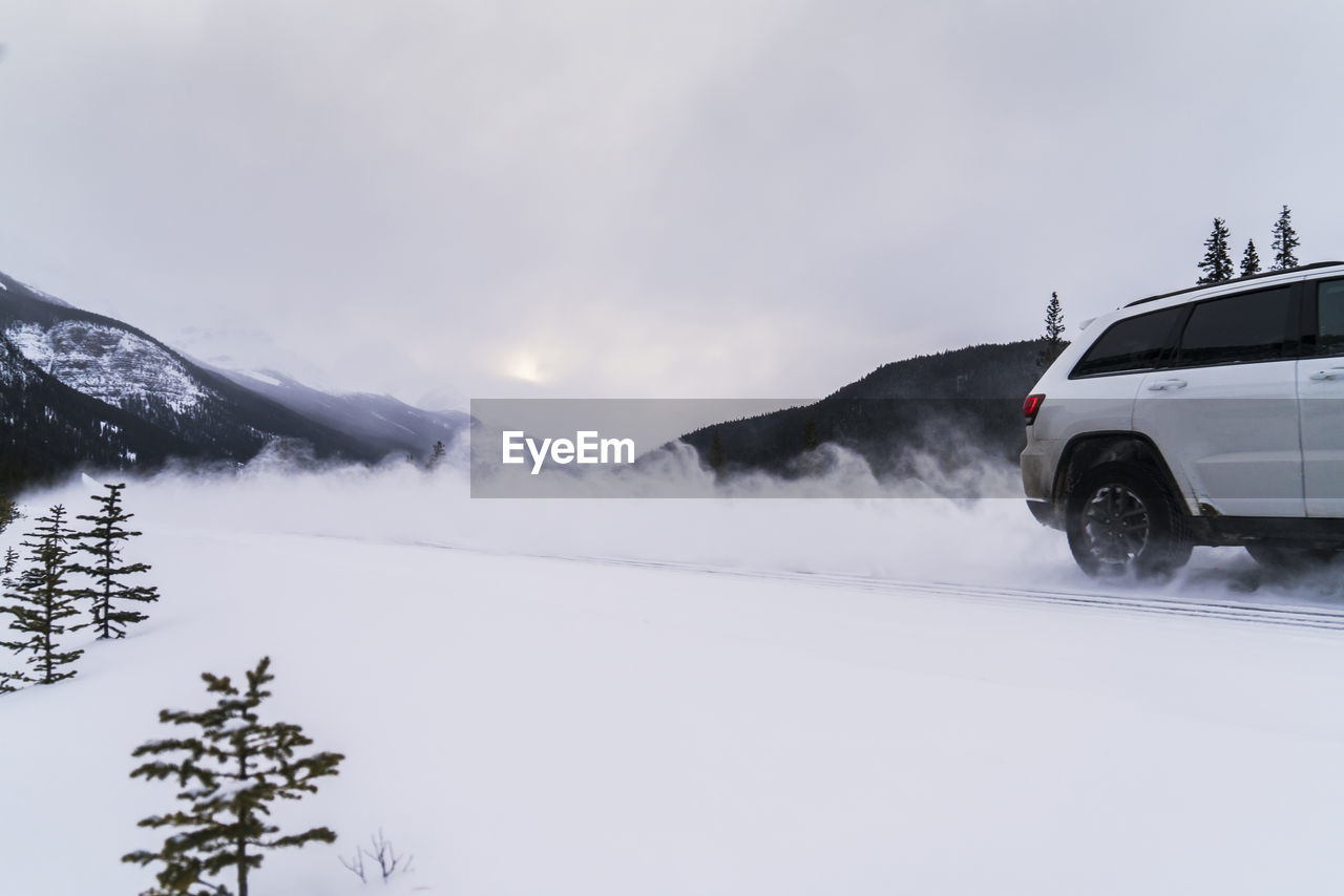 Off-road vehicle moving on snow covered field against cloudy sky