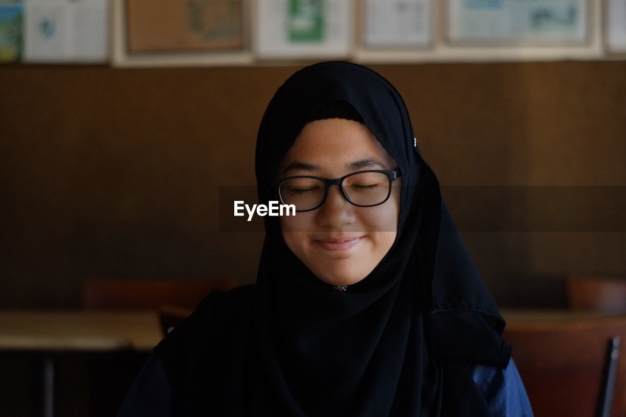 Close-up of happy girl wearing hijab and eyeglasses with closed eyes at restaurant