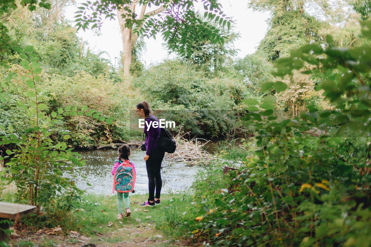 Full length of mother and daughter standing by river in forest