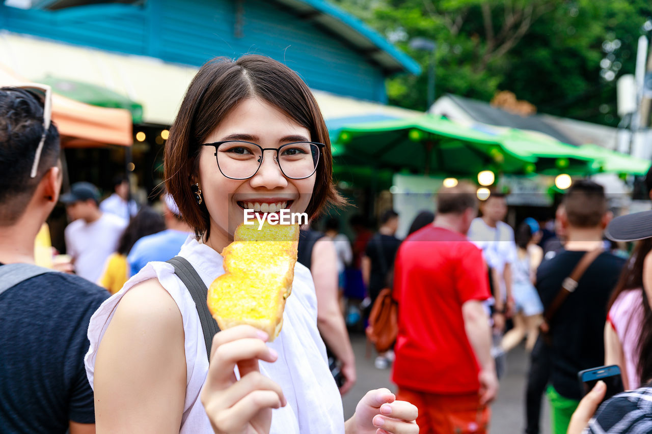 Asian young short hair beautiful woman wearing glasses enjoy eating butter toast at street market