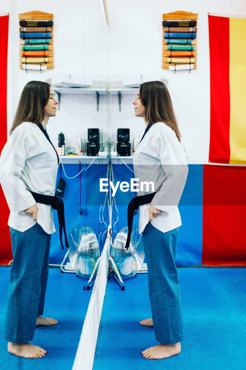 Side view of woman in sports clothing standing in front of mirror