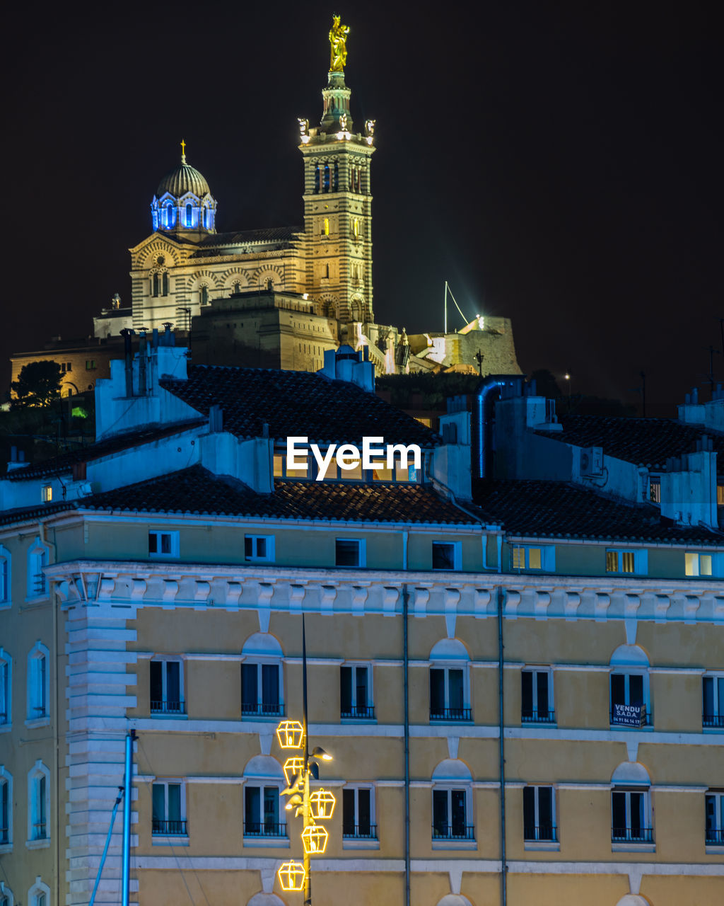 Illuminated basilica of notre dame de la garde overlooking marseille old port at night, france