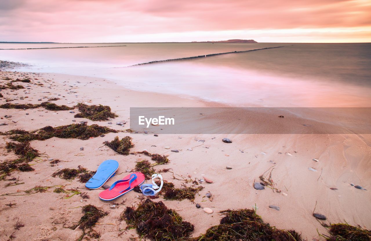 Blue red flip flops and white swimming goggles ready for using on stony beach at wooden breakwater