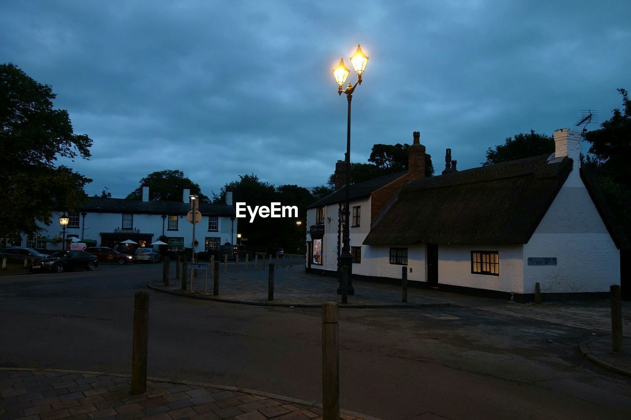 Illuminated lights amidst houses and road at dusk