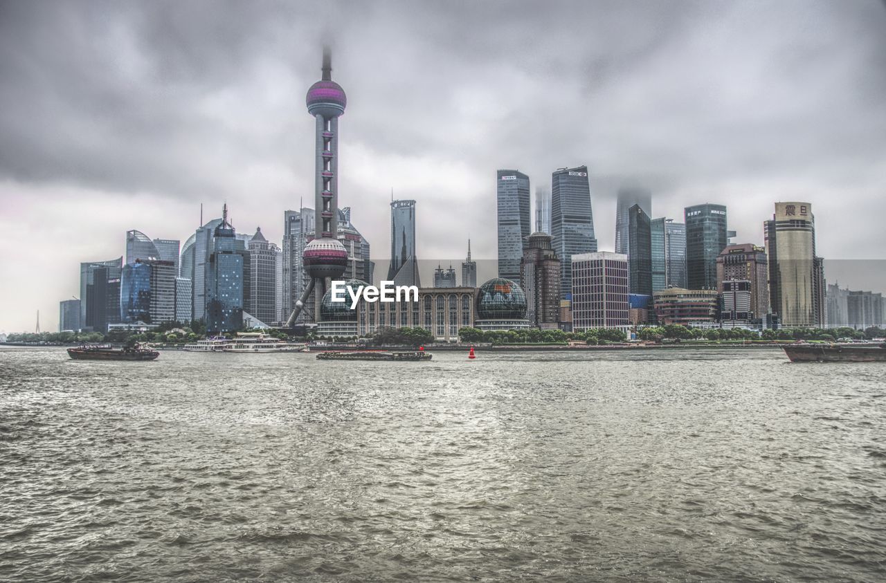 Modern buildings by river against cloudy sky