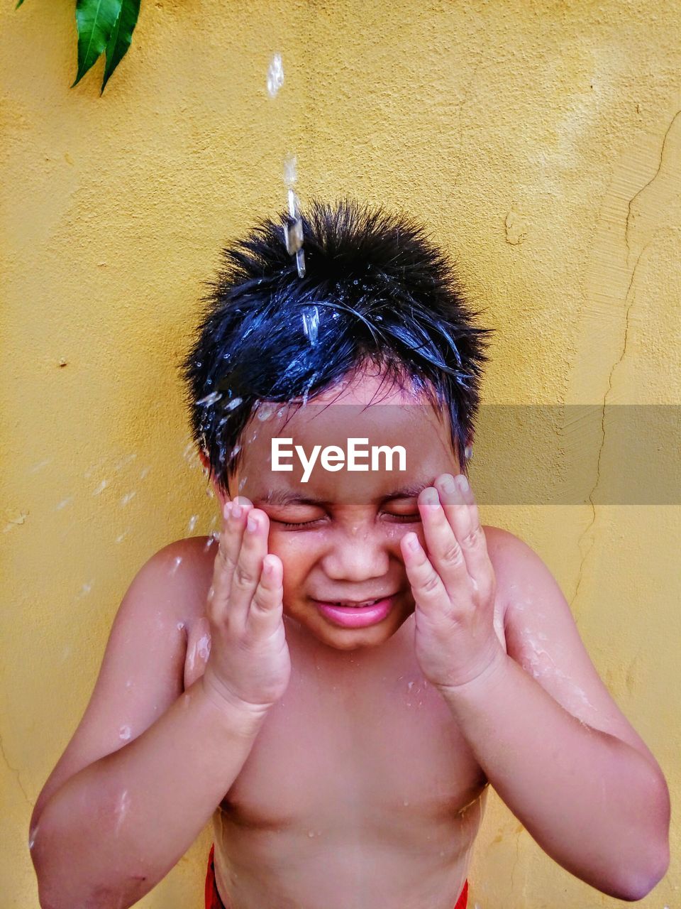 High angle view of water splashing on shirtless boy standing against wall