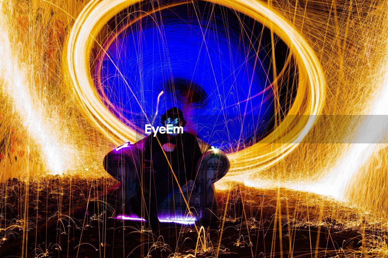 Spooky man sitting on armchair surrounded by light trails at night