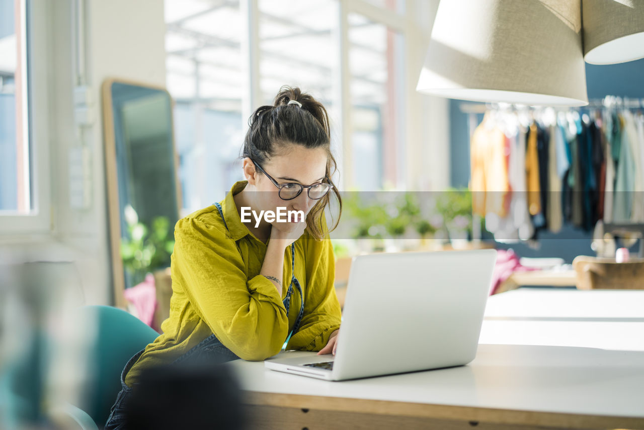 Fashion designer sitting at desk in her studio looking at laptop