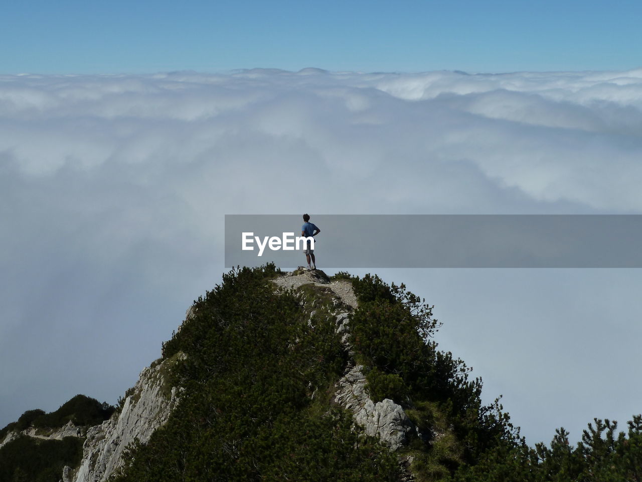 LOW ANGLE VIEW OF PERSON STANDING ON MOUNTAIN AGAINST SKY