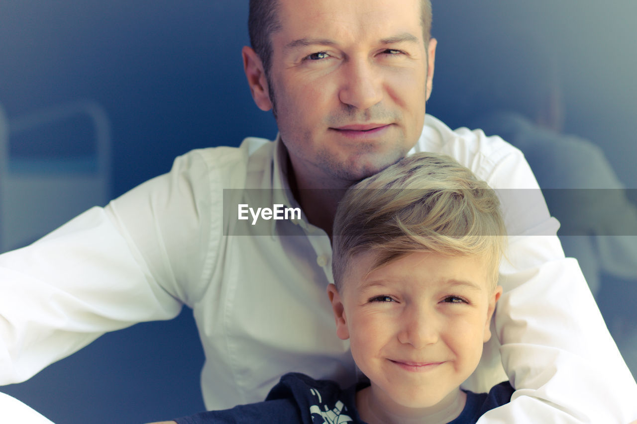 Portrait of happy father and son against wall