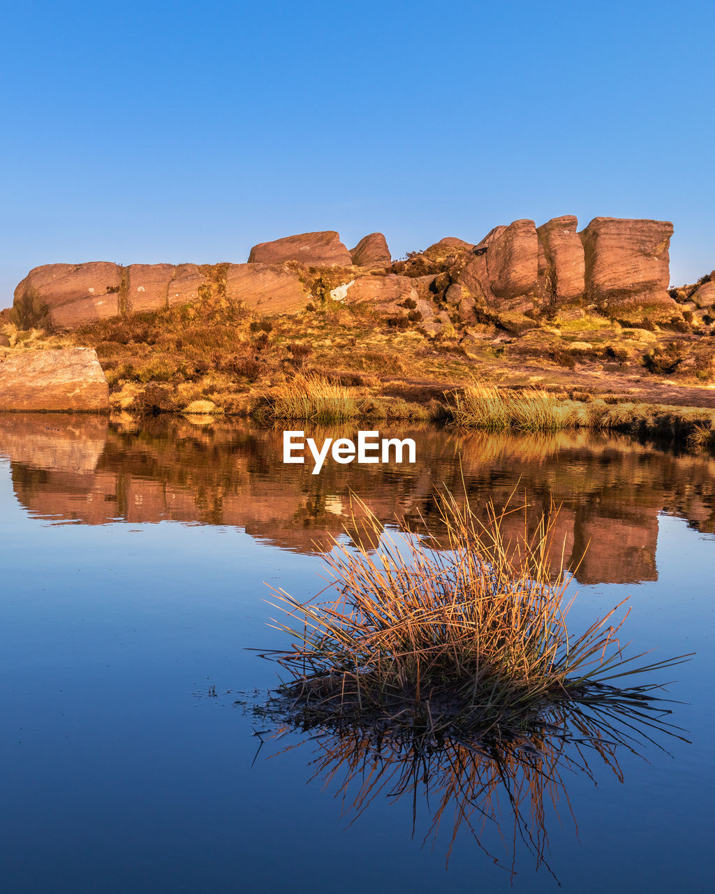 Reflection of rock formation in water against clear blue sky