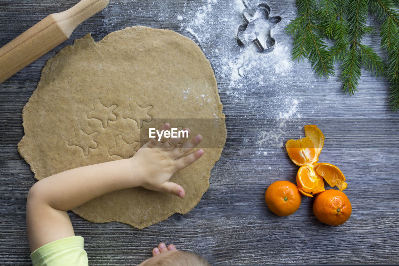 A small child and cooking gingerbread cookies in a kitchen with tangerines and a christmas tree.