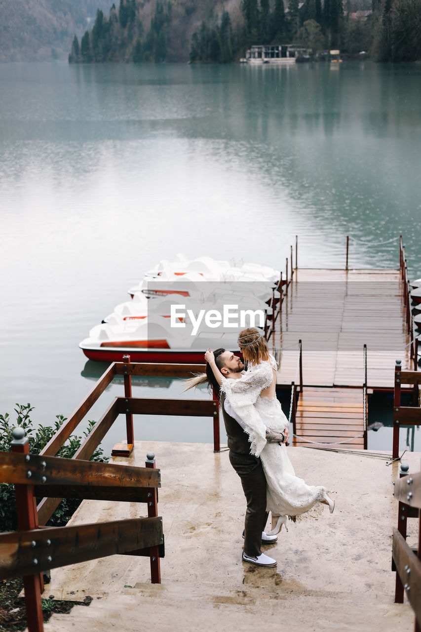 A loving married couple bride and groom in suits celebrate their wedding near the mountains water