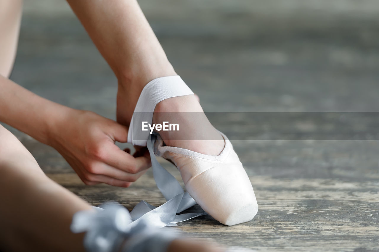 Cropped image of woman wearing ballet shoe on floor