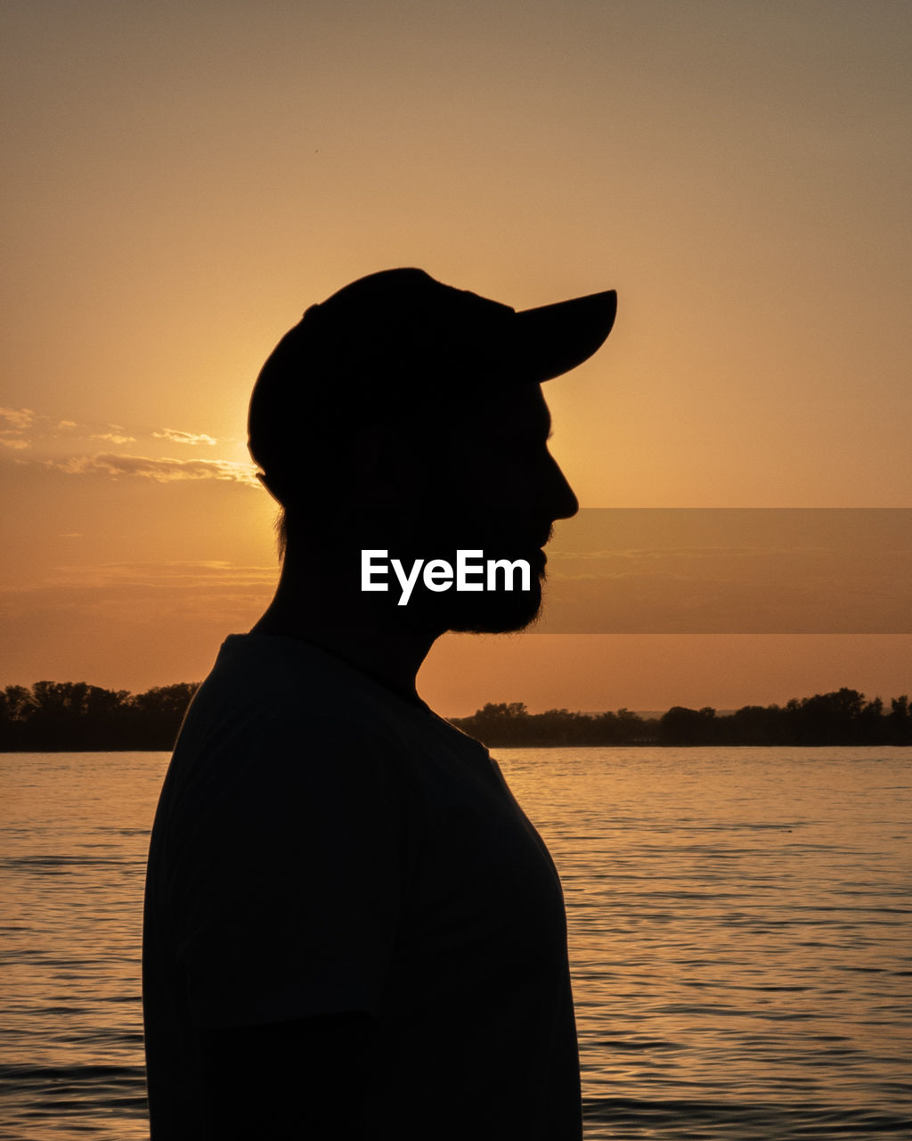 Silhouette man standing by lake against sky during sunset