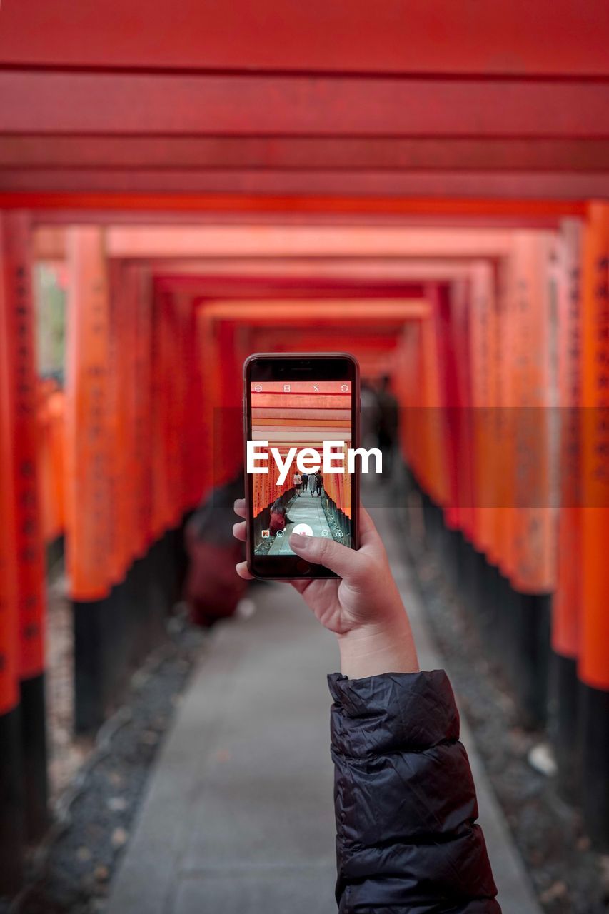 Cropped hand of person photographing shrine with mobile phone