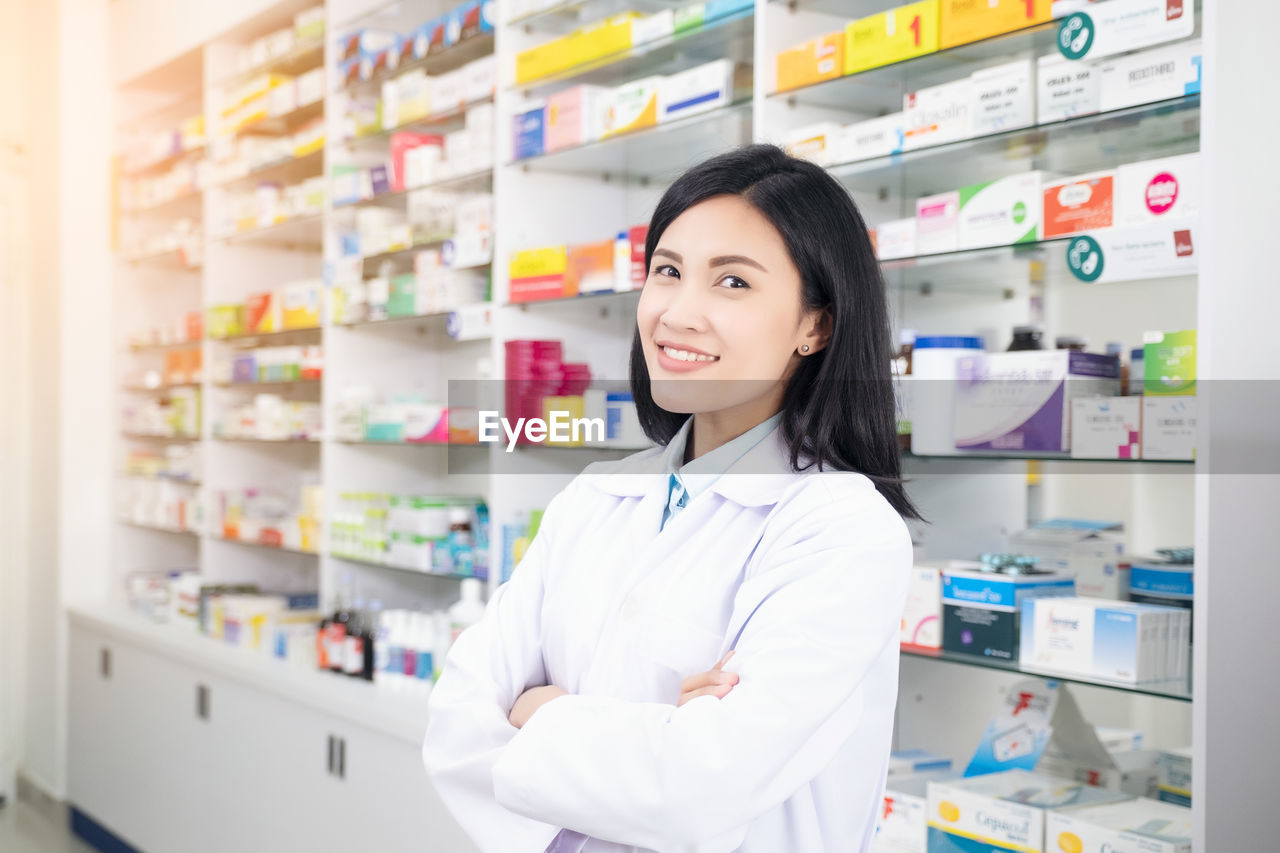 PORTRAIT OF A SMILING YOUNG WOMAN STANDING AT STORE