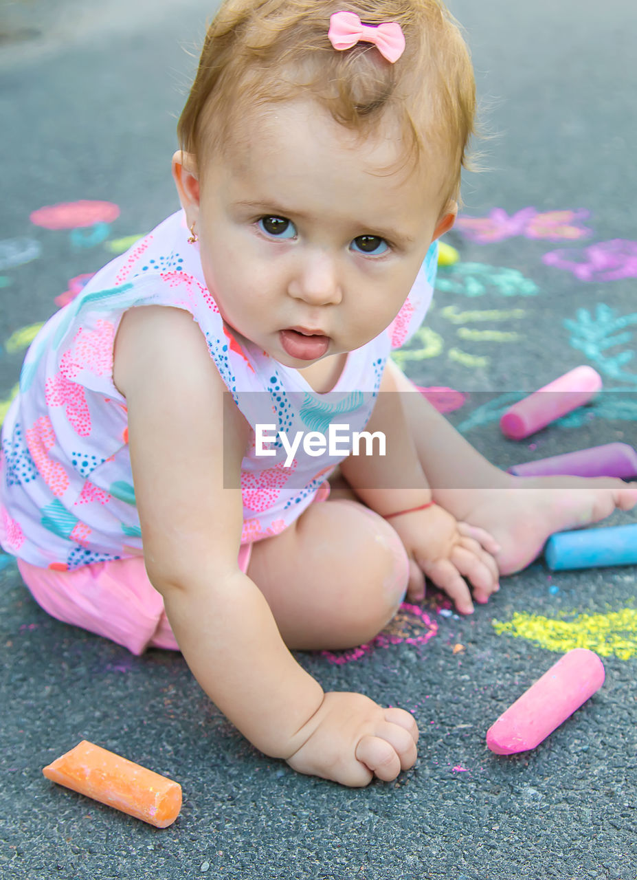 Cute baby with chalk sitting on sidewalk