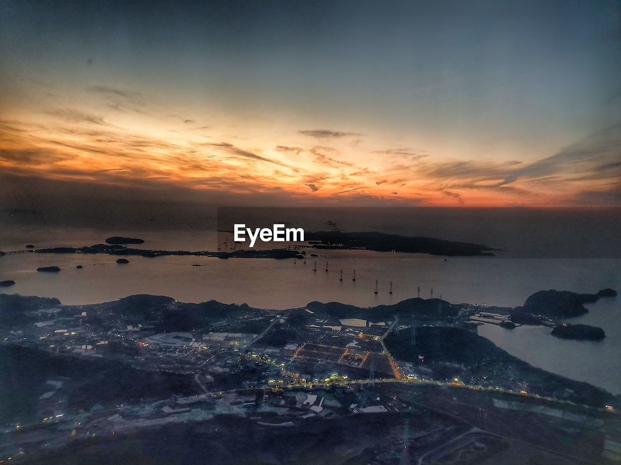 HIGH ANGLE VIEW OF TOWNSCAPE AND SEA AGAINST SKY AT SUNSET