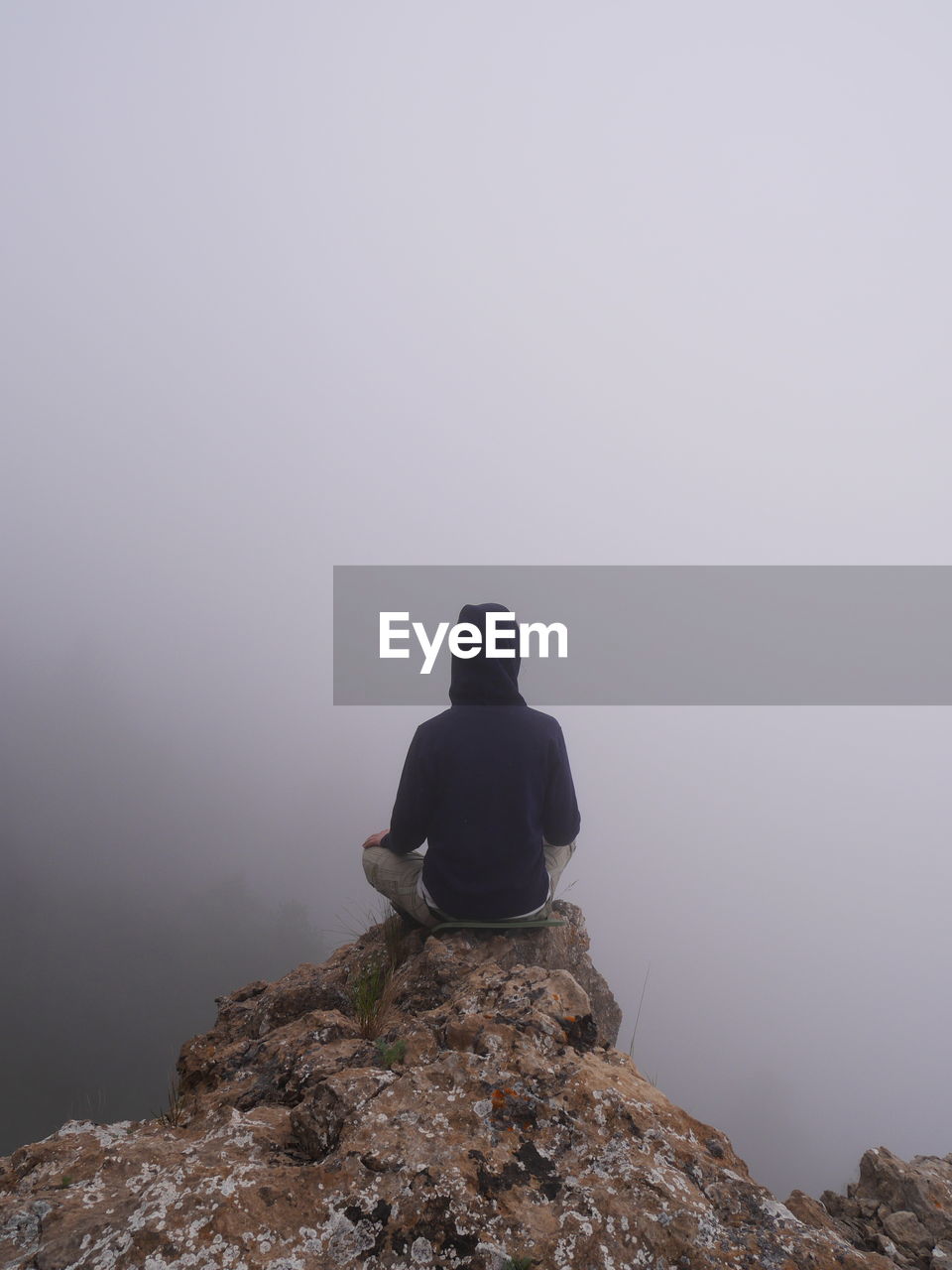 Rear view of person sitting at the edge of cliff during foggy weather