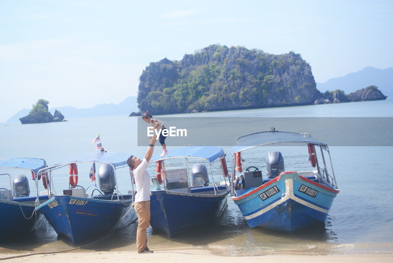 MAN STANDING IN SEA AGAINST MOUNTAINS