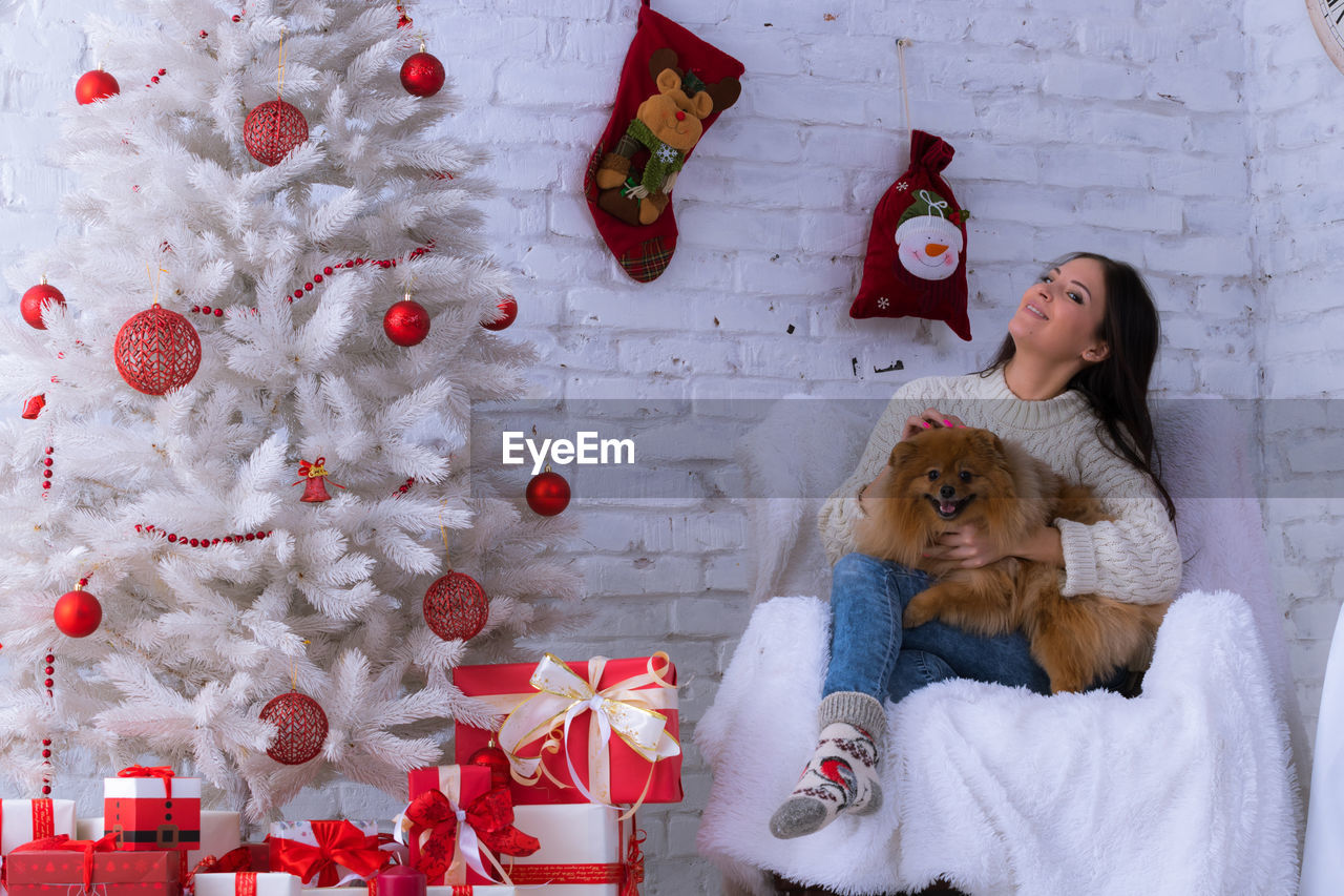 Woman embracing dog while sitting on chair during christmas