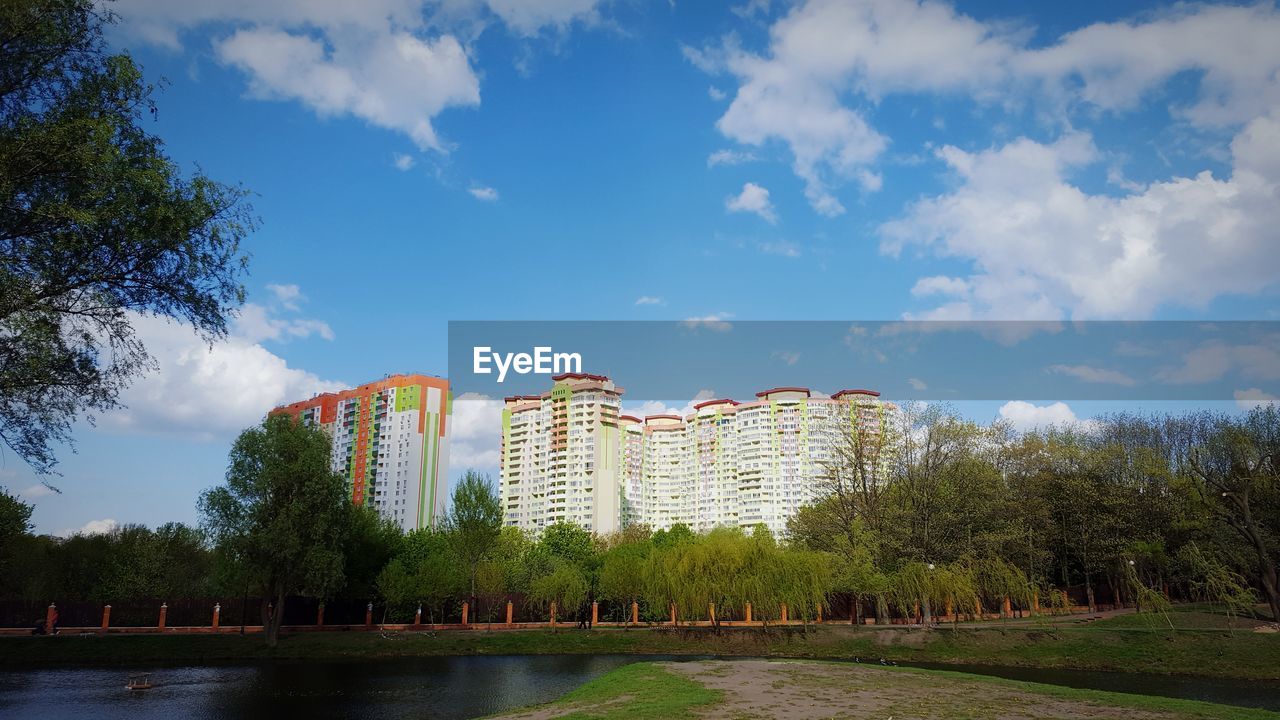 View of buildings by lake against cloudy sky