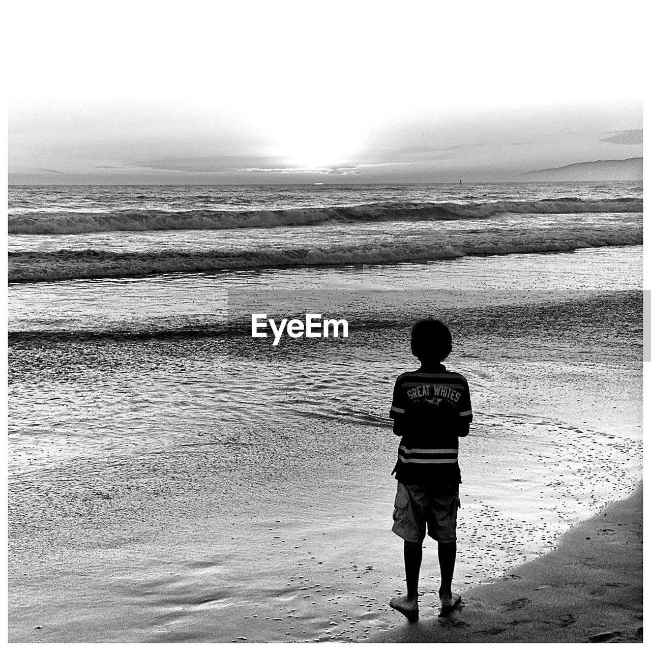 Rear view of boy standing on beach during sunset
