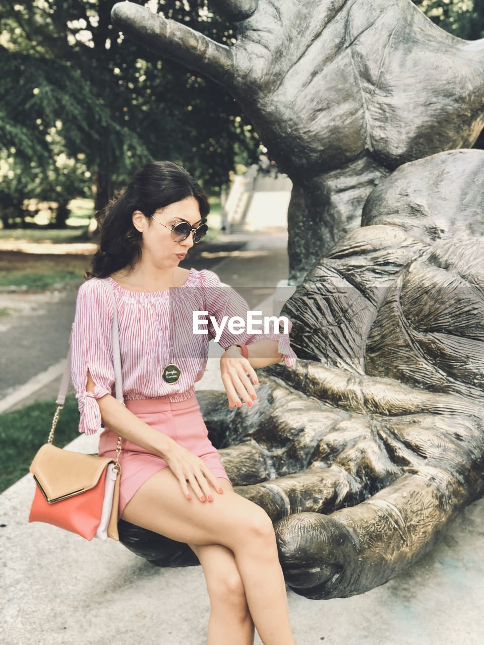 Woman sitting on hand of statue while looking at wristwatch