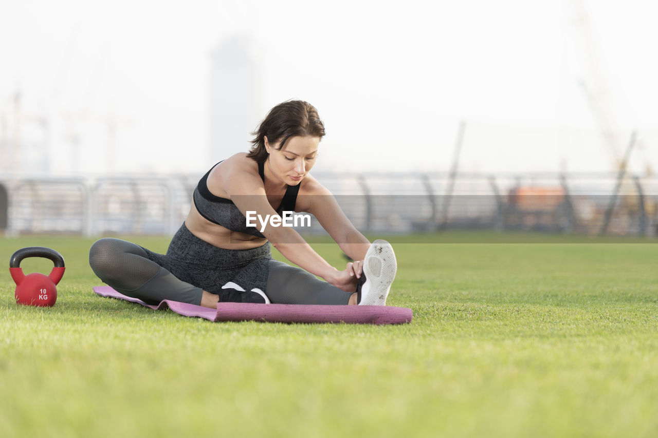 Full length of young woman exercising while sitting over mat on grass