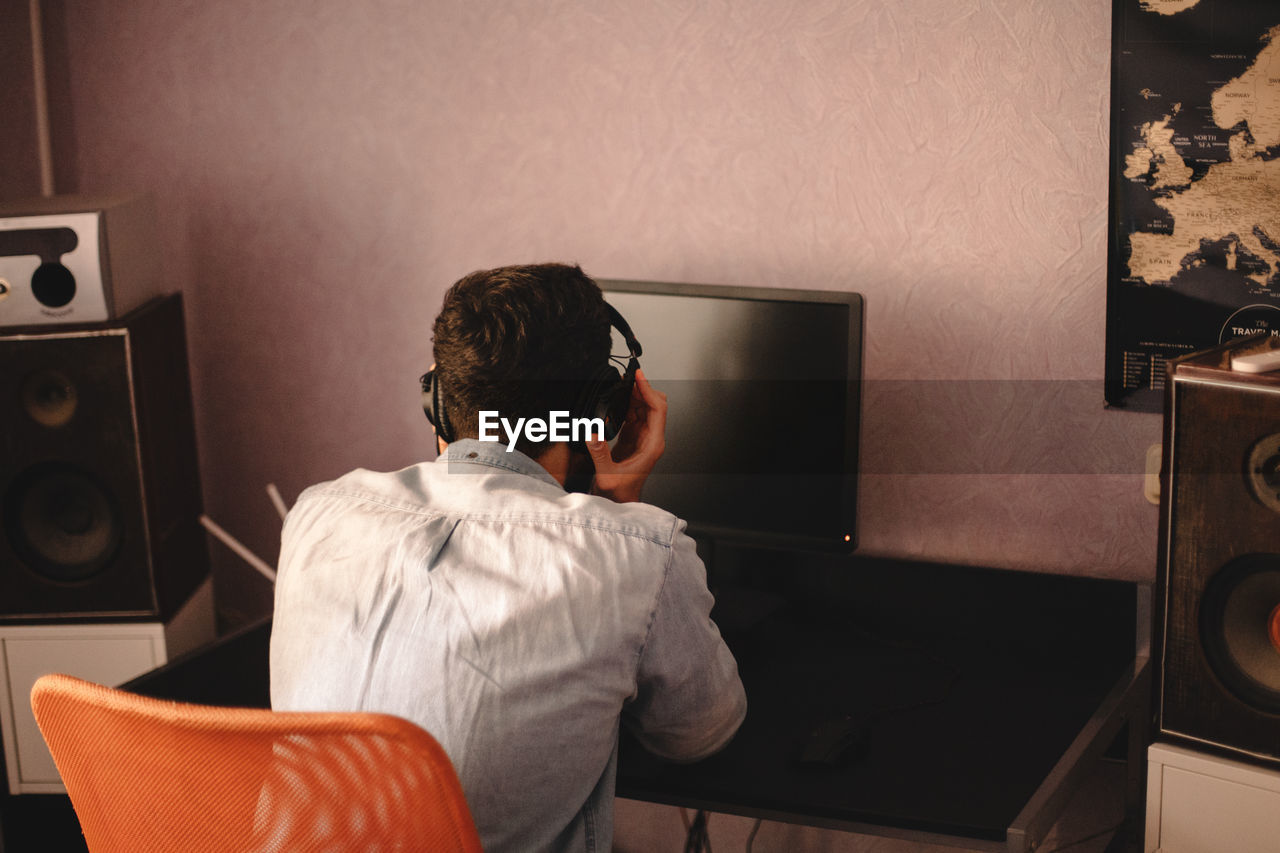 Man holding headphones while listening music sitting by computer