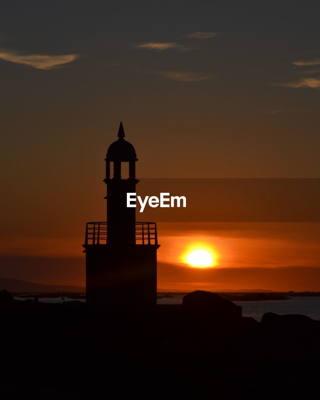 Silhouette lighthouse by sea against sky at sunset