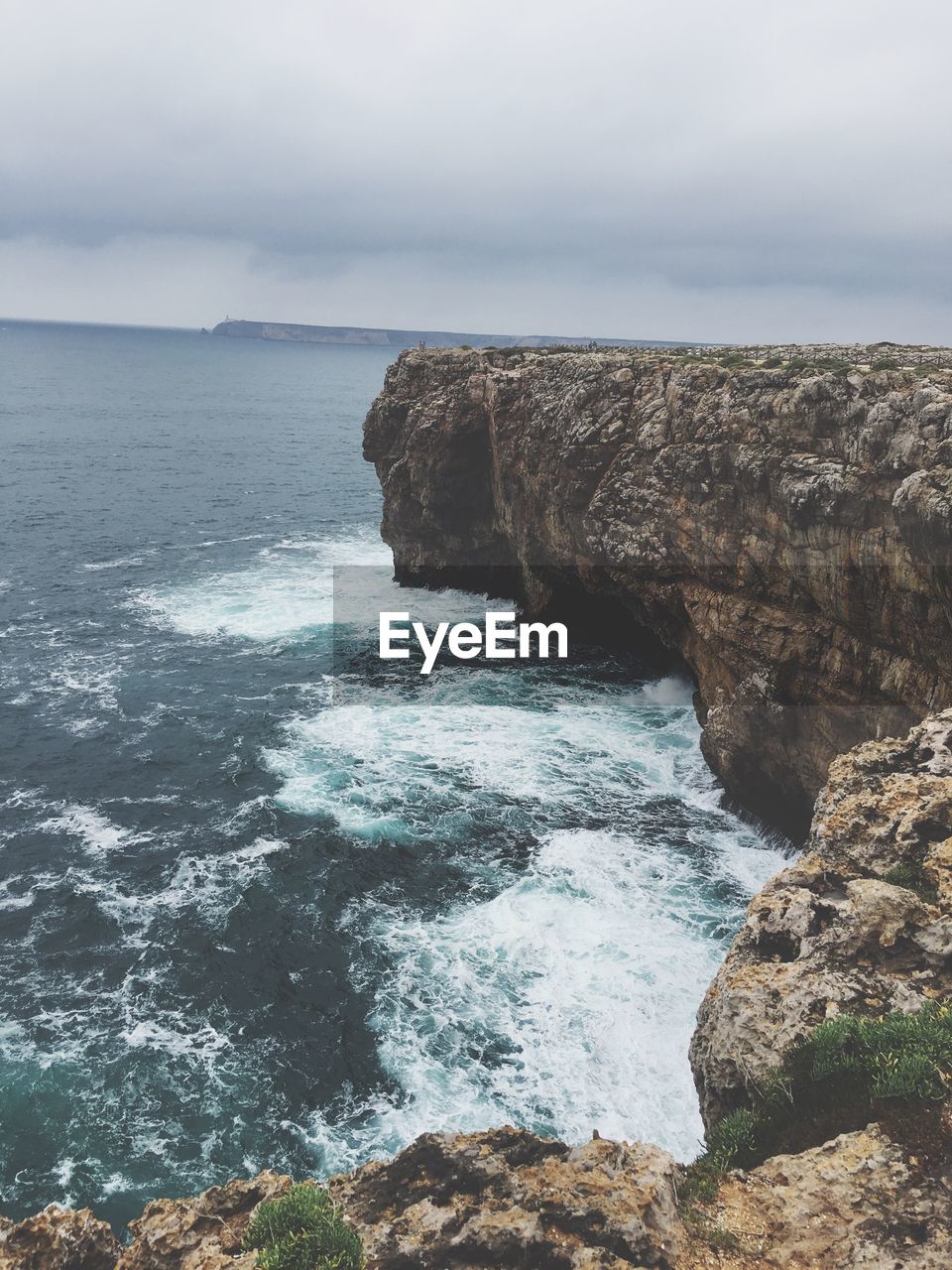 Scenic view of cliff at sea shore against cloudy sky