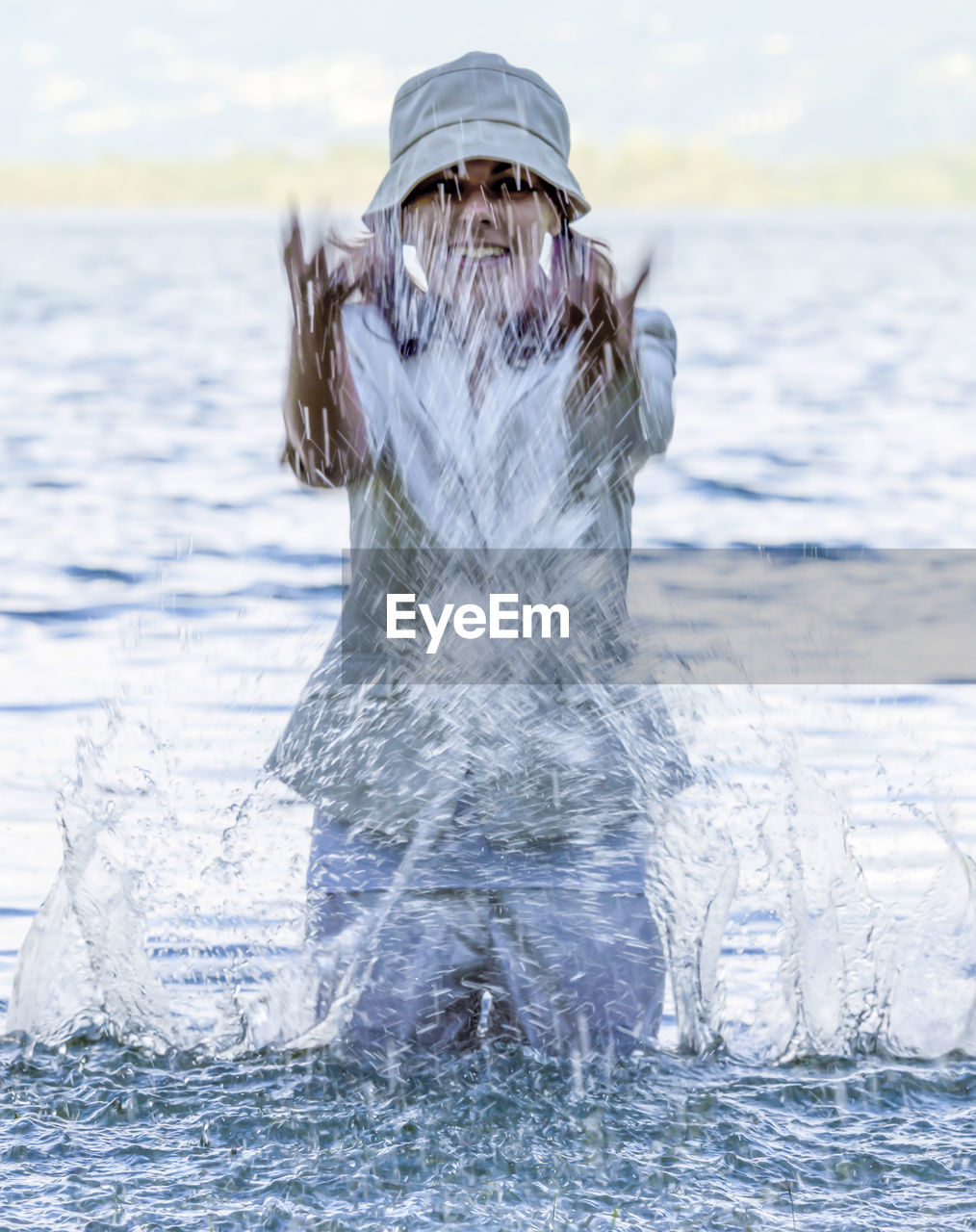 Woman with clothes and hat standing and splashing in the water in locarno, switzerland.
